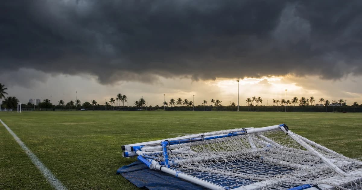 Storm clouds gathering over an empty Miami soccer field with a folded portable goal at the sideline illustrating hurricane preparedness for youth soccer clubs.